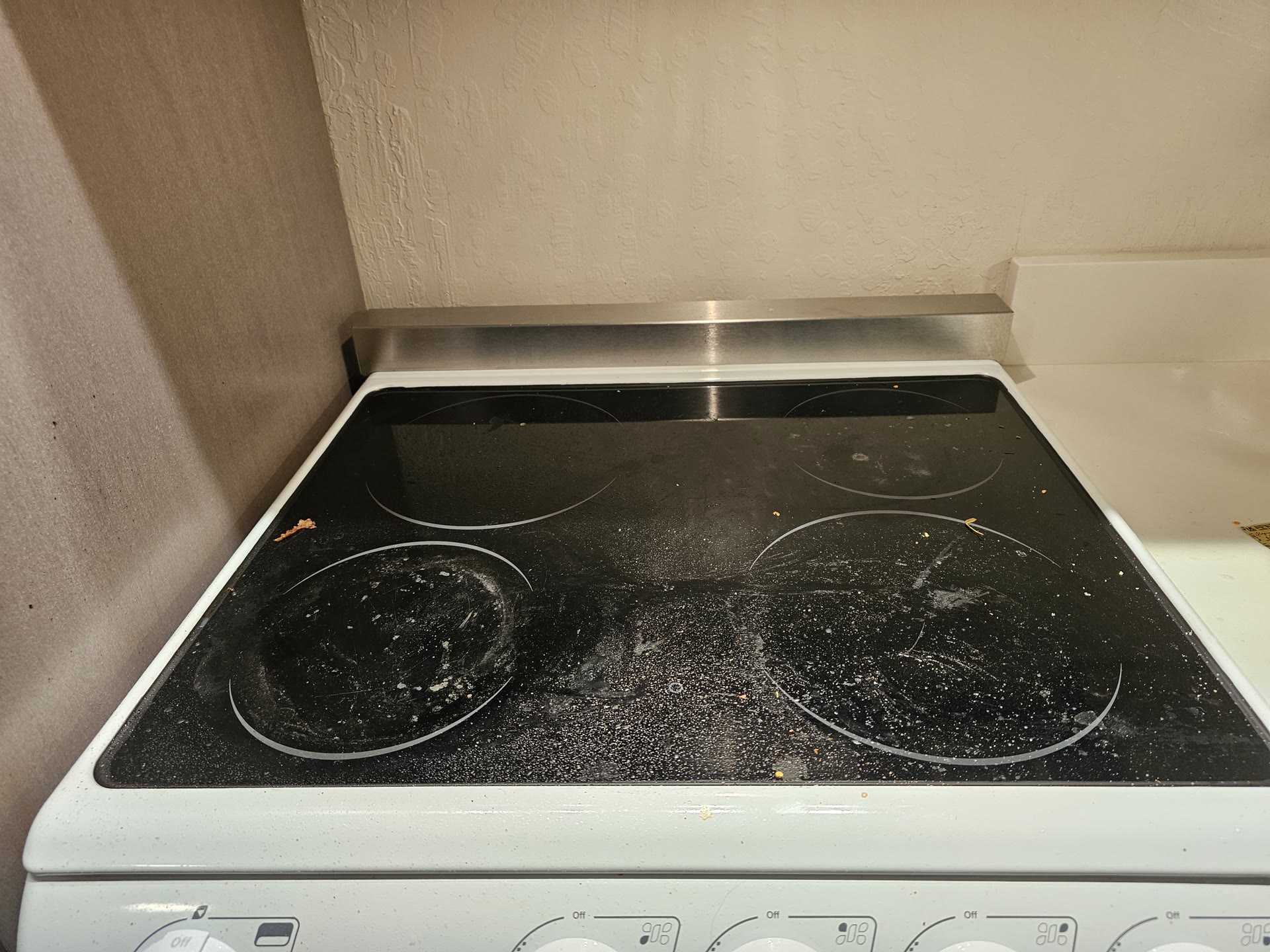 A glass cooktop covered in crumbs and dried spills before a cleaning